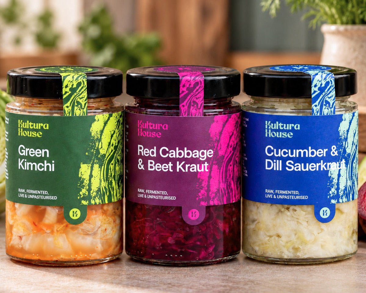 Three jars of Kultura House naturally fermented vegetables: Green Kimchi, Red Cabbage & Beet Kraut, and Cucumber & Dill Sauerkraut, displayed on a kitchen countertop.